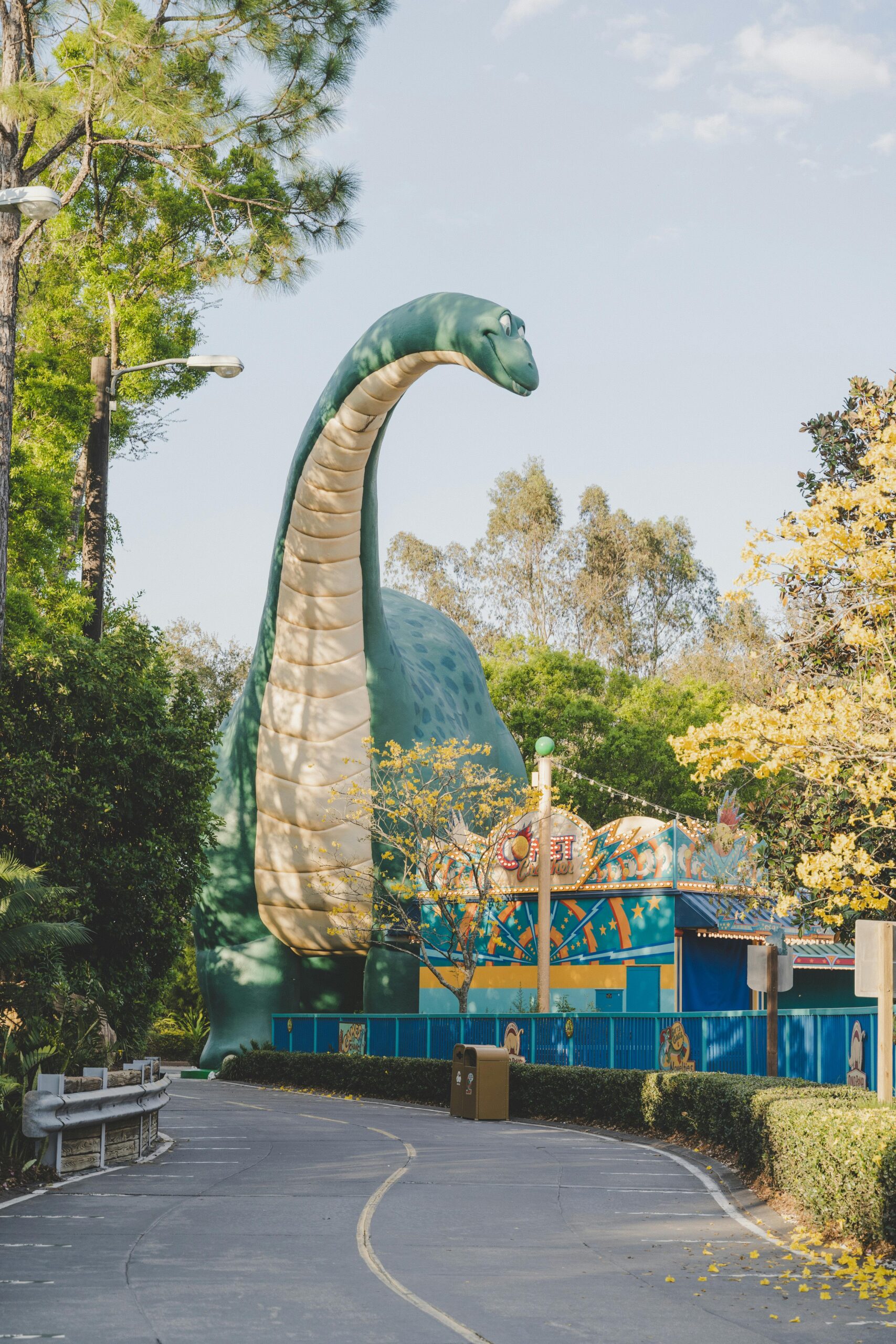 Giant dinosaur sculpture in a theme park surrounded by greenery and pathways.