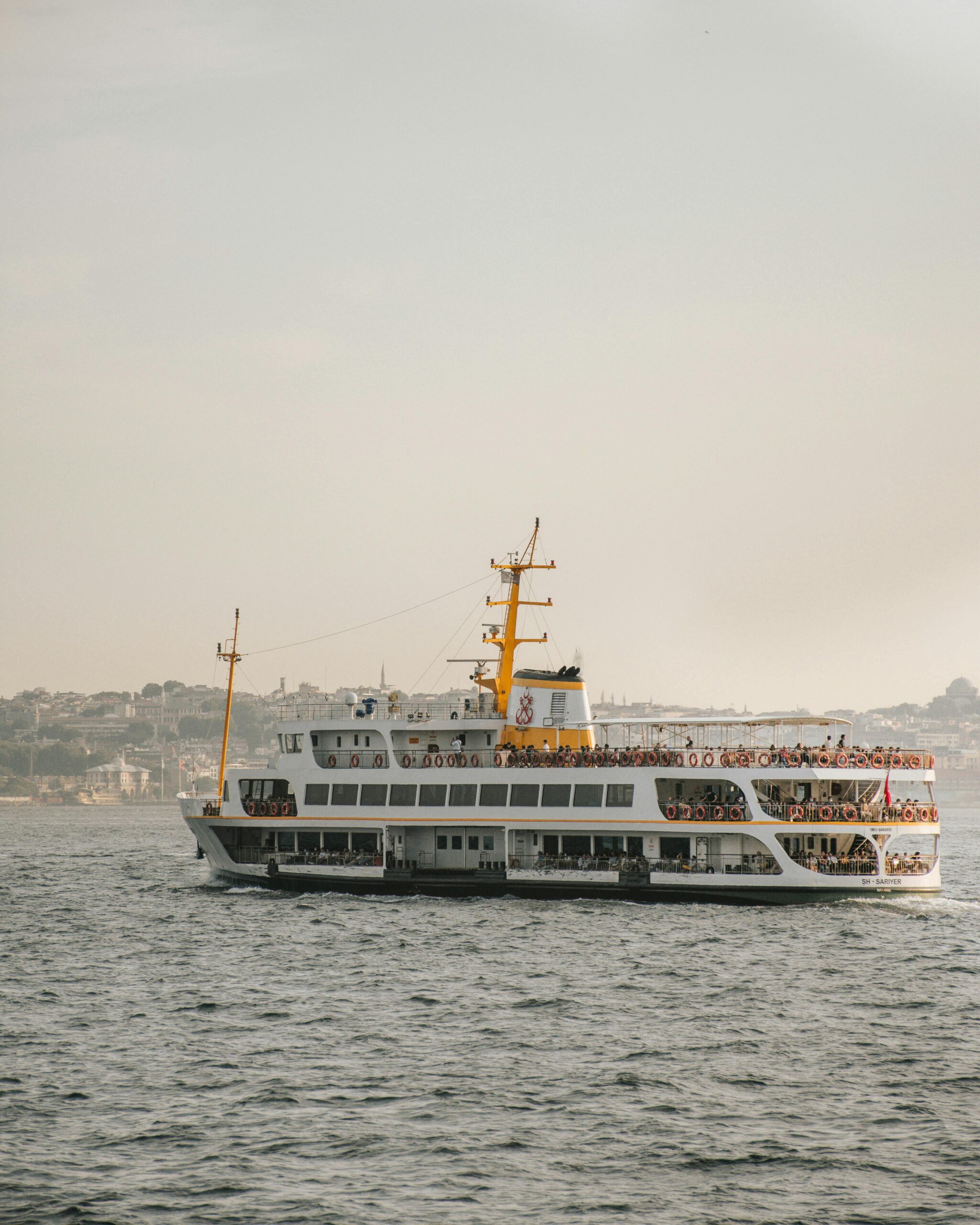 A bustling cruise ship full of tourists sailing on a calm sea under a clear sky.